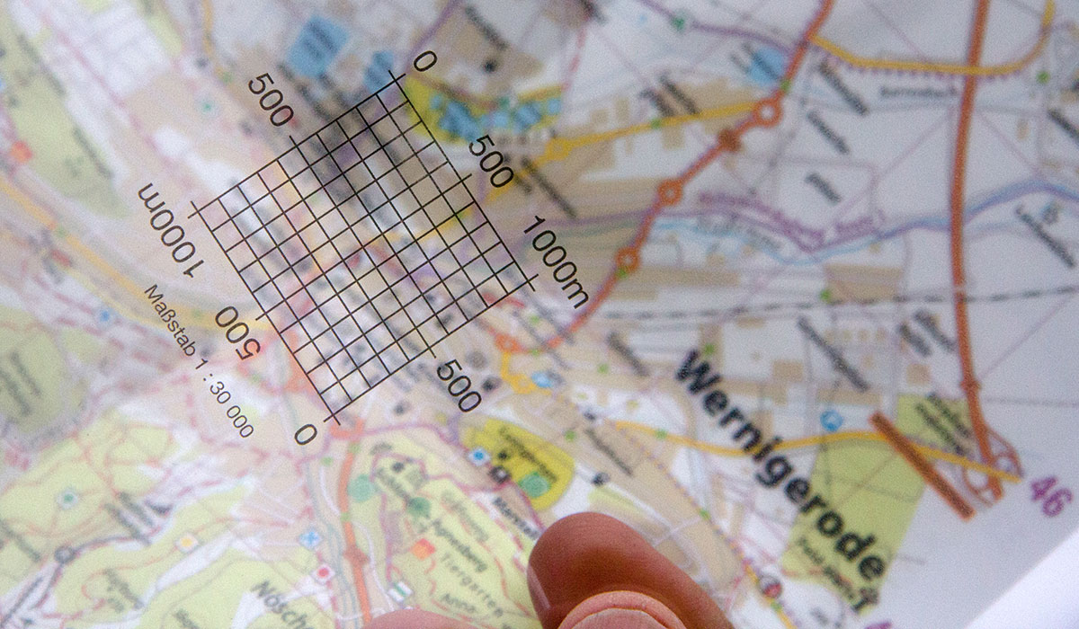 Eine Hand hält ein auf eine Folie gedrucktes Kartometer über eine Harz-Wanderkarte