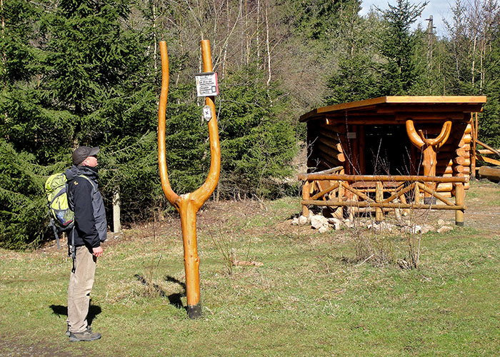Ein Wanderer steht vor einer Schutzhütte und schaut auf ein Wanderschild