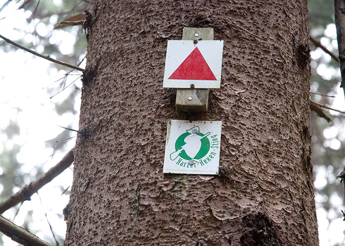 An einem Baum hängt ein Hexen-Stieg-Schild und ein rotes Dreieck.
